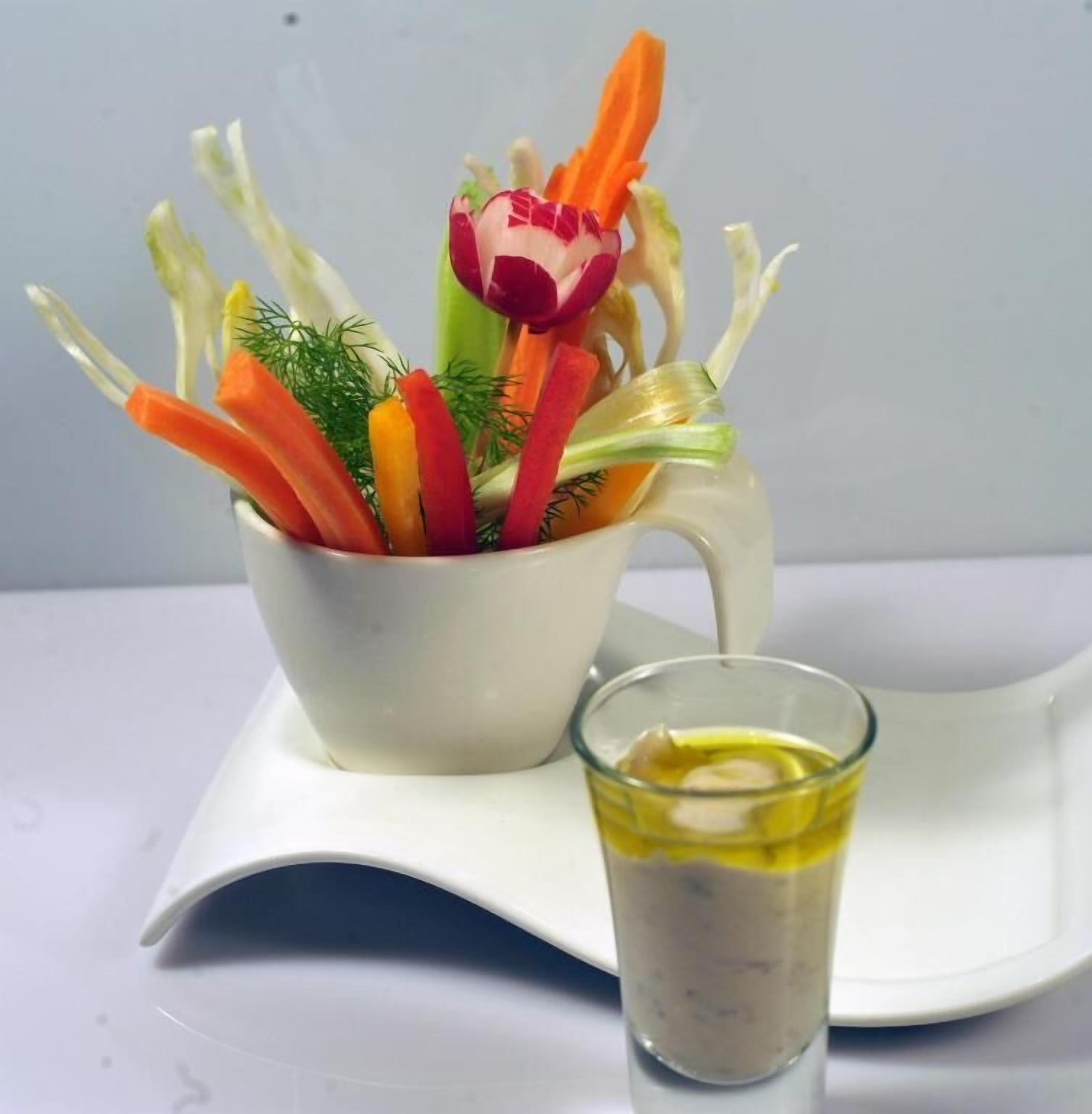 Un tazón de cerámica blanca lleno de verduras variadas y un vaso de aderezo sobre un plato blanco.