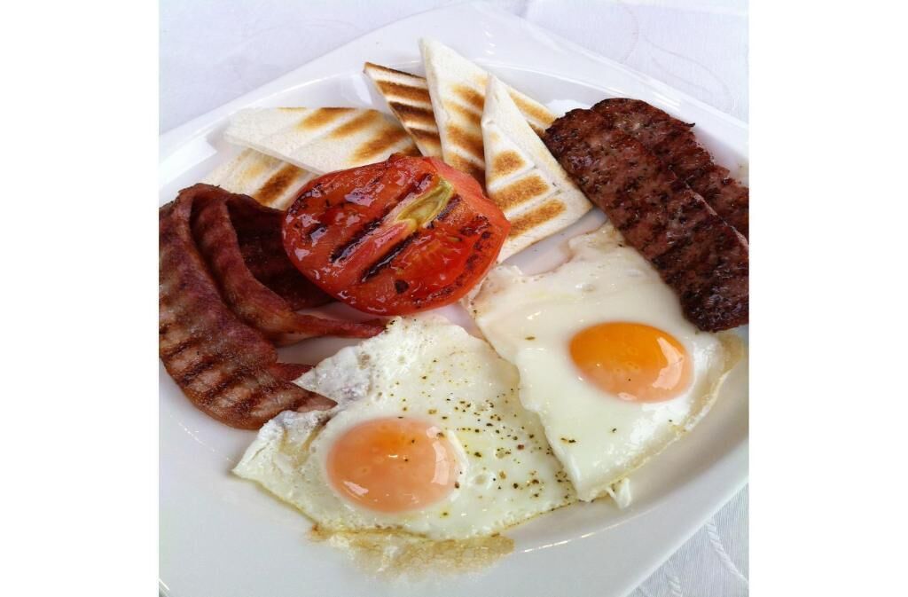 Un plato de desayuno con huevos, tocino, salchichas, tomates a la parrilla y tostadas.