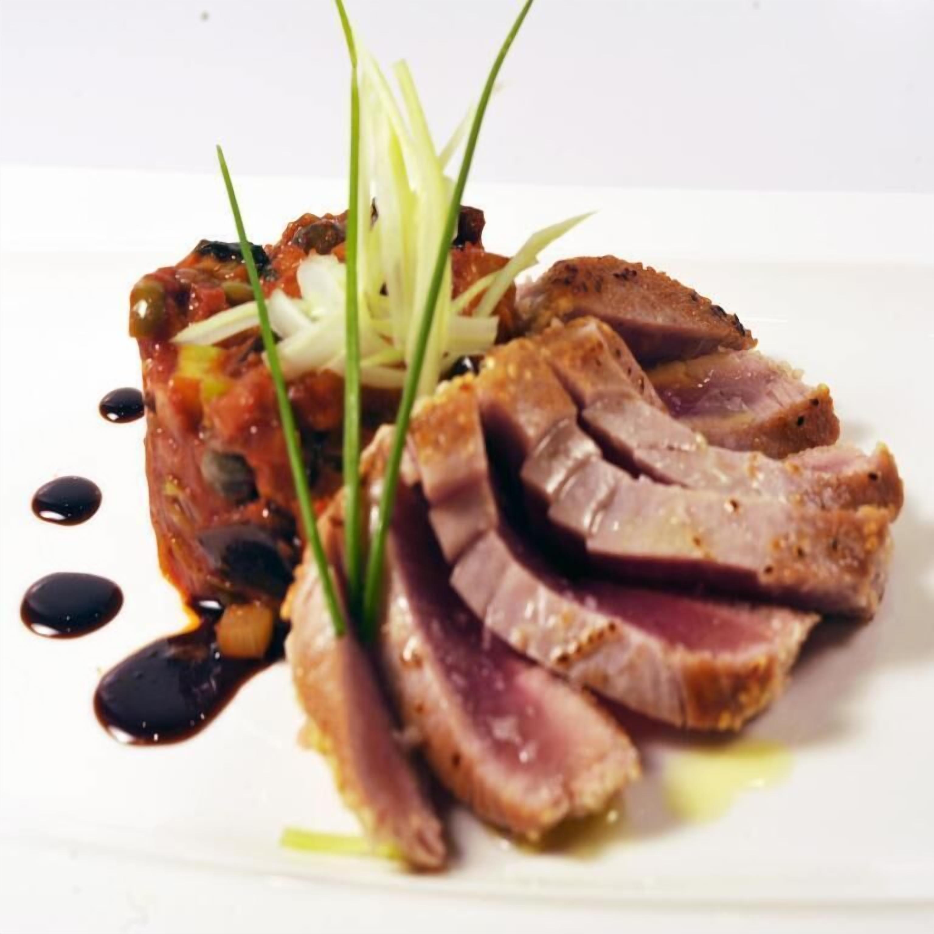 A plate with sliced meat, vegetables, and a sauce.