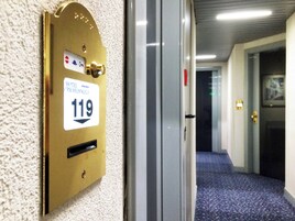 Puerta de una habitación de hotel con una placa de latón con el número 119 y una cerradura.