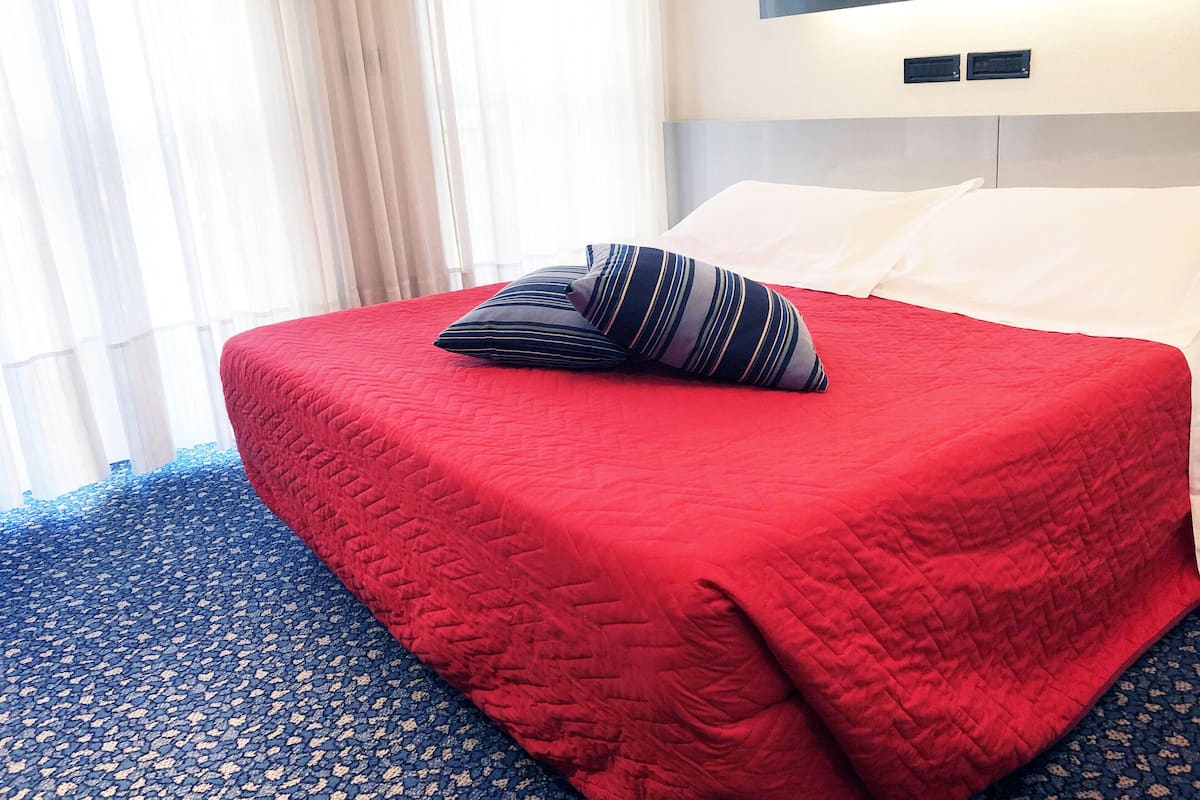 Une chambre d’hôtel avec une couvre-lit rouge, un coussin à rayures et une tête de lit dotée d’un éclairage intégré.