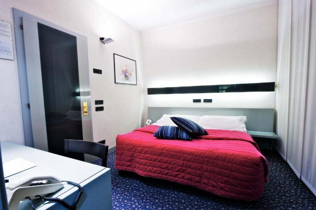 A hotel room with a bed, a desk, a chair, and a door.