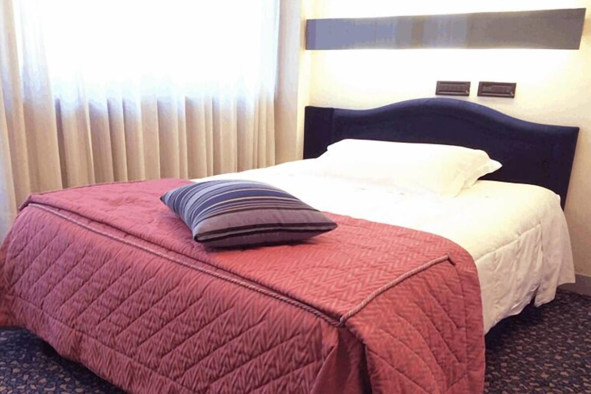 Un lit bien fait, avec une couette rouge, un oreiller rayé et un oreiller blanc.
