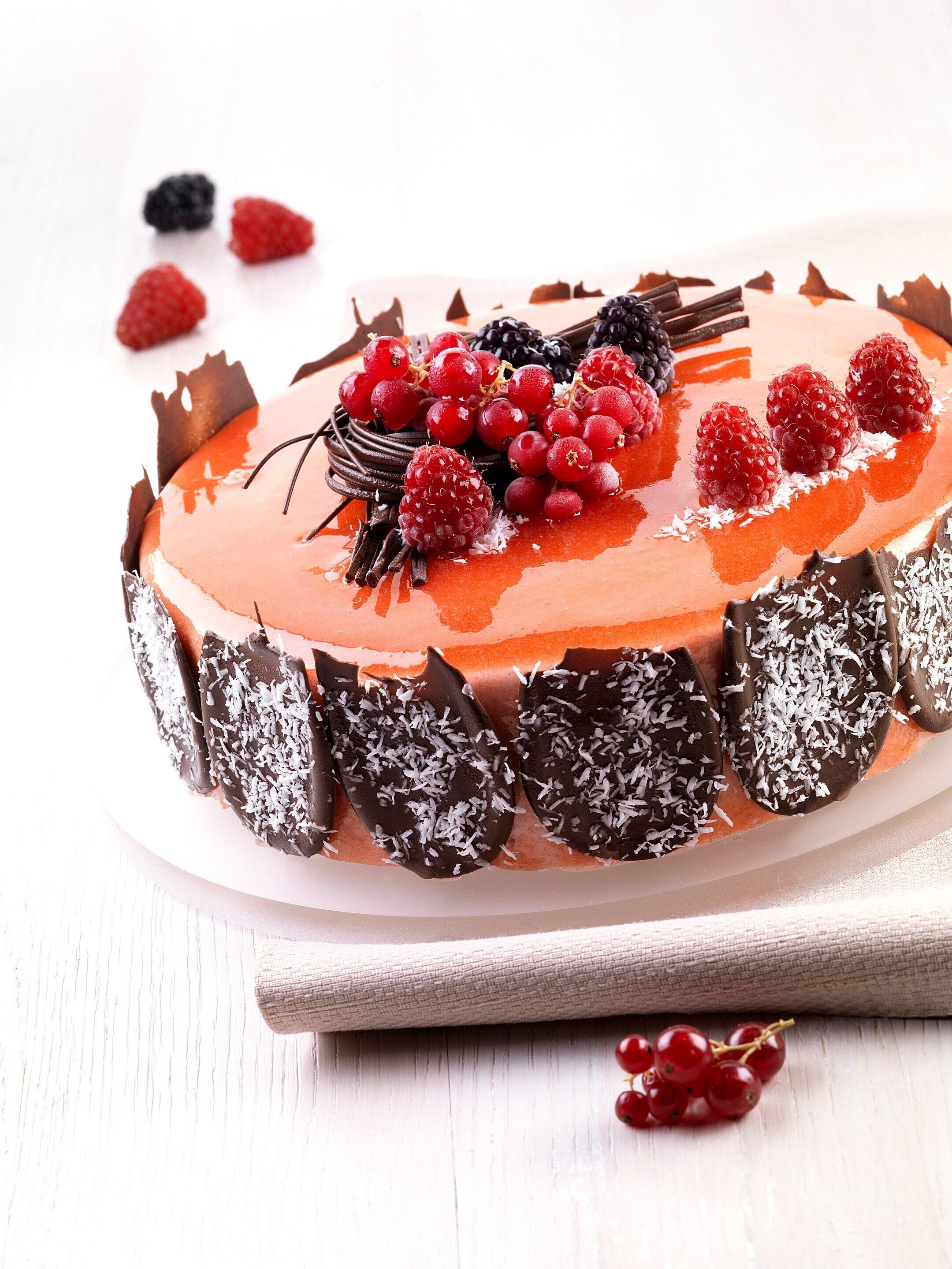 A round cake with red berries and chocolate decorations on a white plate.