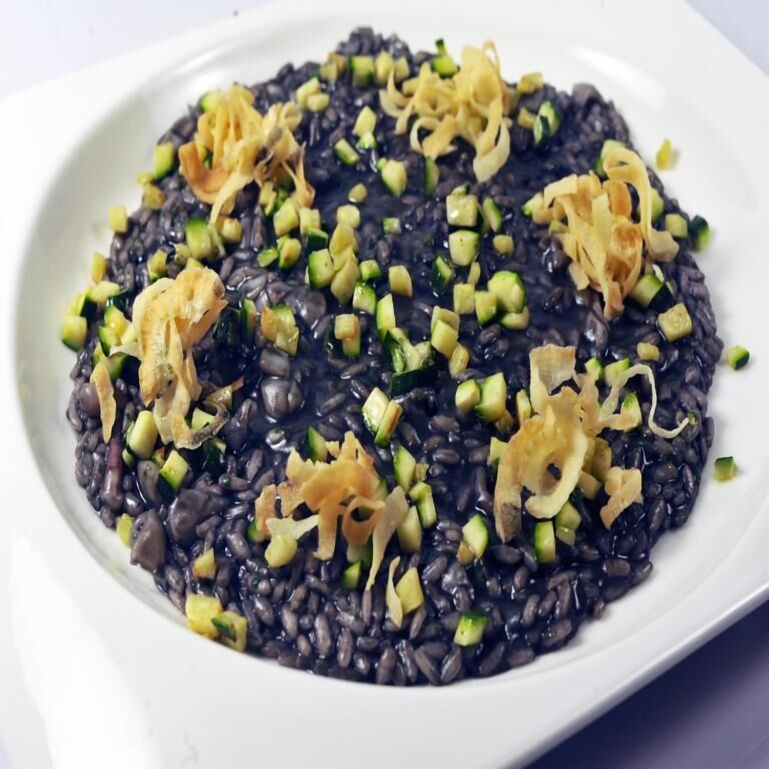 Un piatto di riso nero con zucchine a cubetti e cipolle fritte.