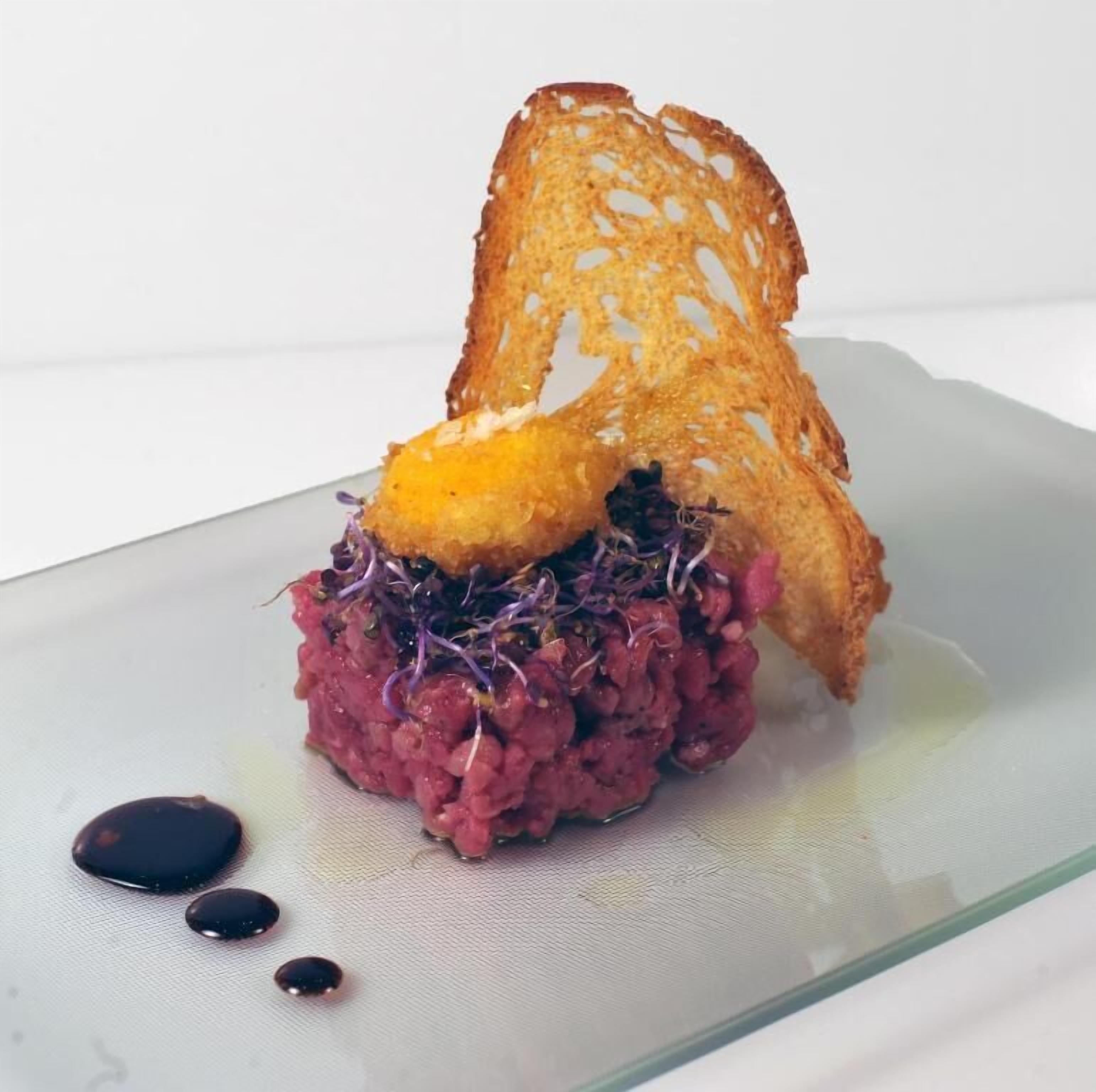 A dish with a toasted bread piece on top, served on a glass plate with a sauce drizzle.