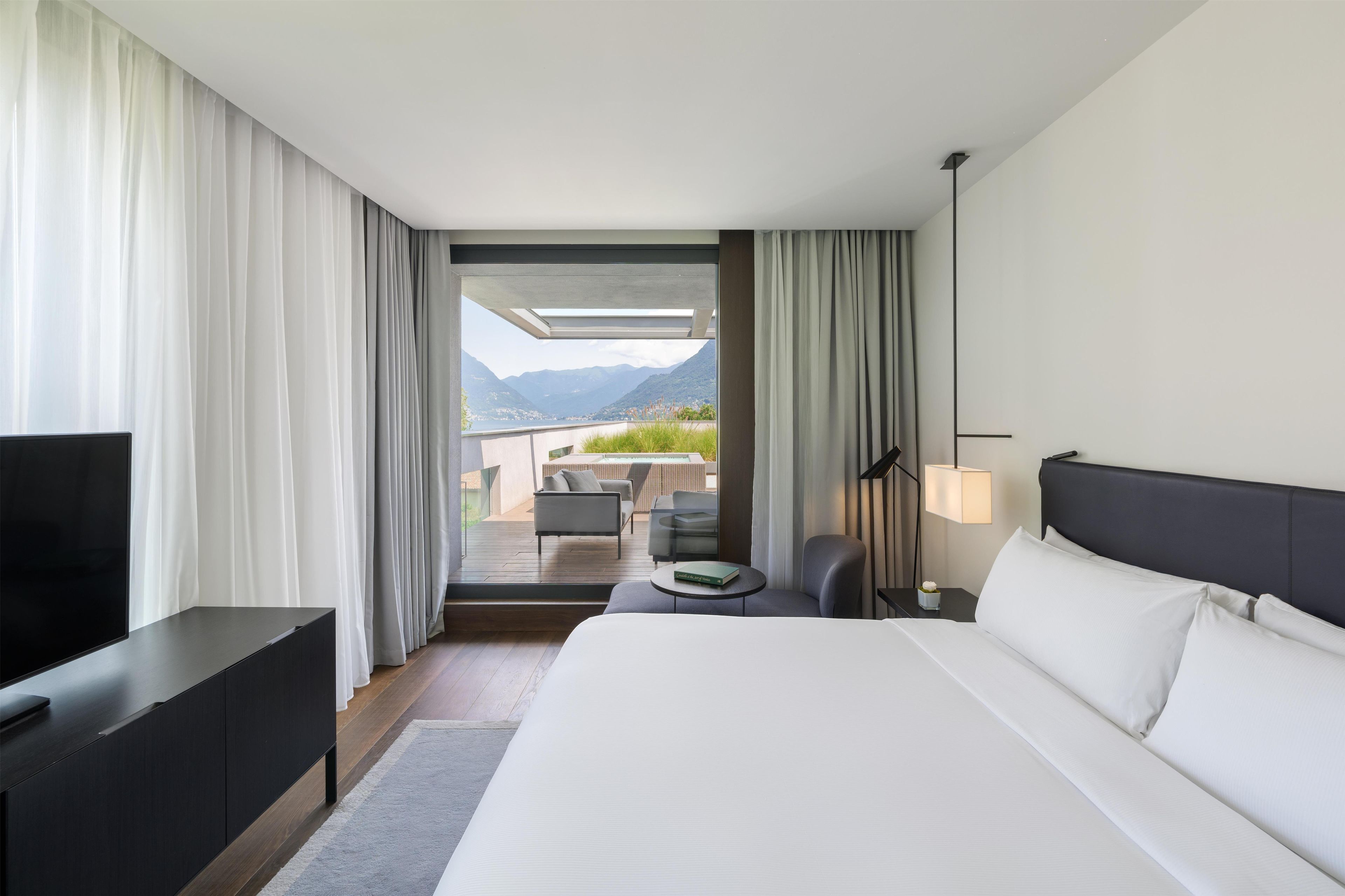 Ein modernes Hotelzimmer mit einem großen Bett, einem Fernseher, einem Schreibtisch und Blick auf Berge.