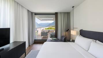 Ein modernes Hotelzimmer mit einem großen Bett, einem Fernseher, einem Schreibtisch und Blick auf Berge.
