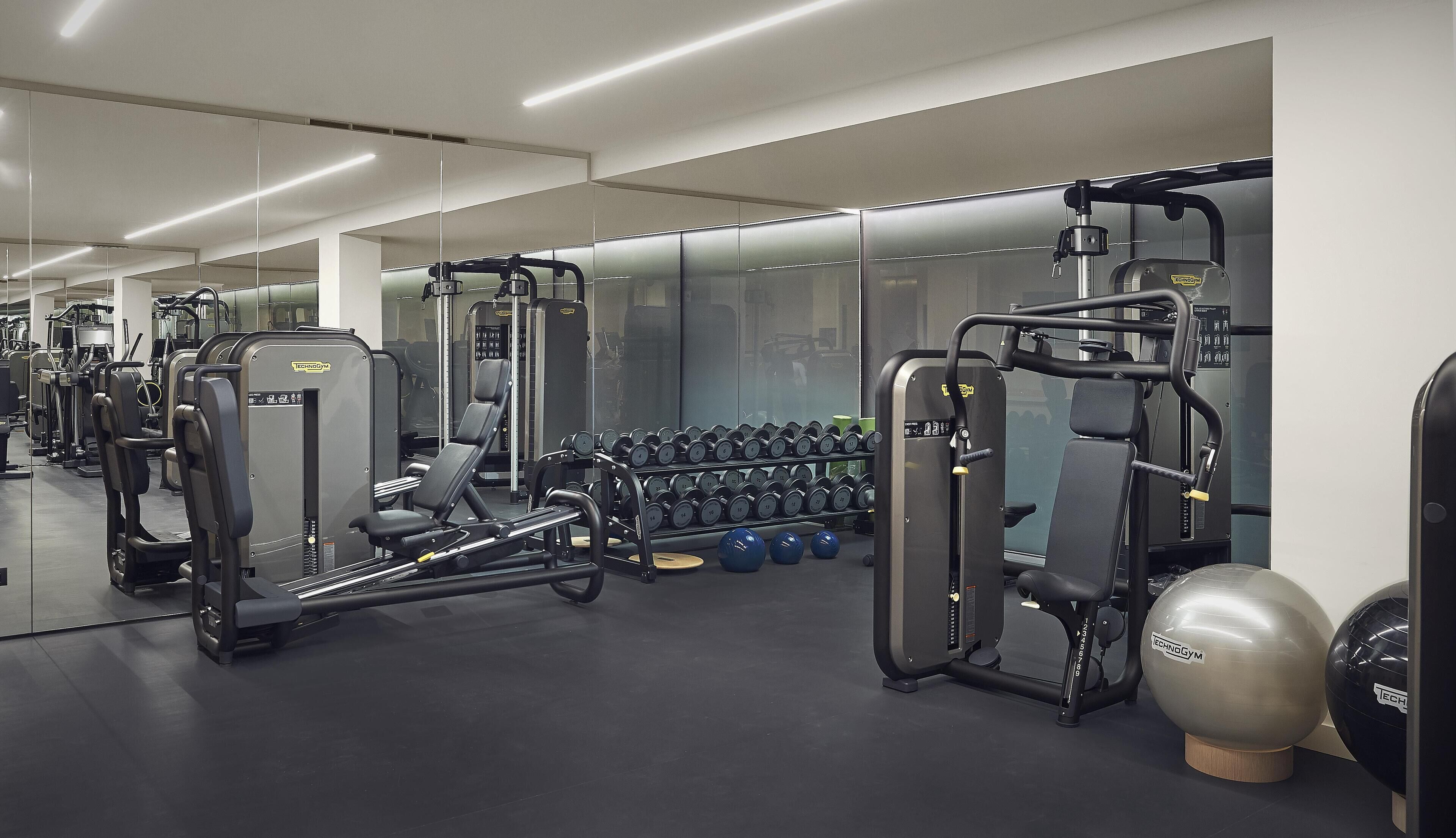 A gym with various exercise machines, dumbbells, and exercise balls.