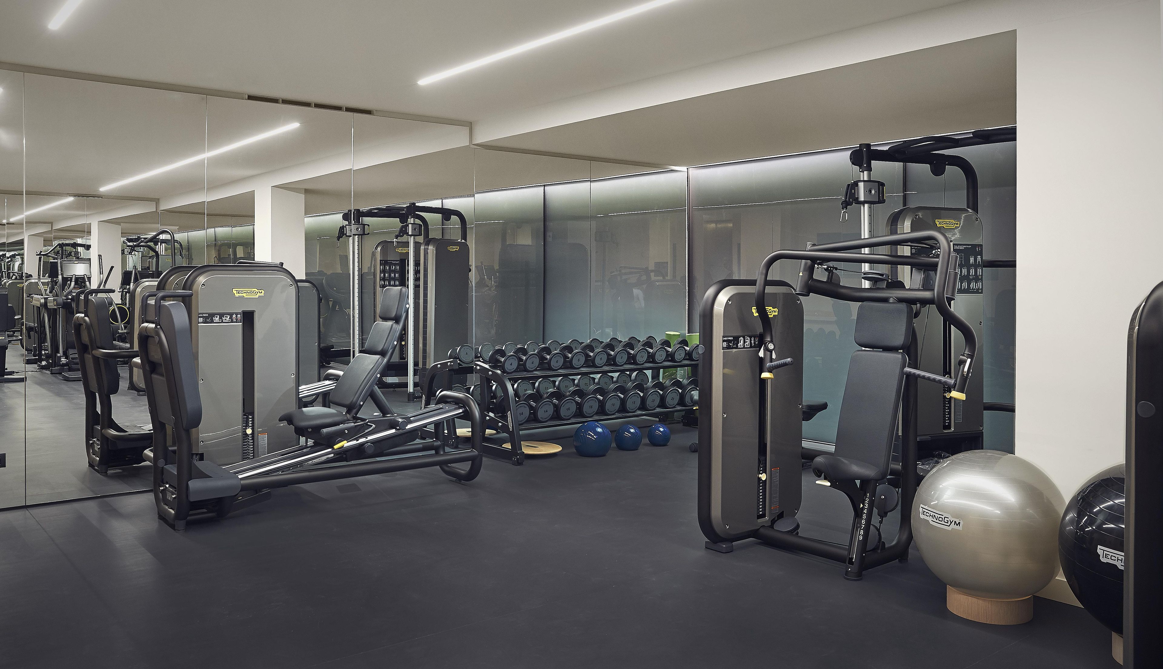 Ein Fitnessstudio mit verschiedenen Trainingsgeräten, darunter Kraftgeräte, Kurzhanteln und Gymbälle.