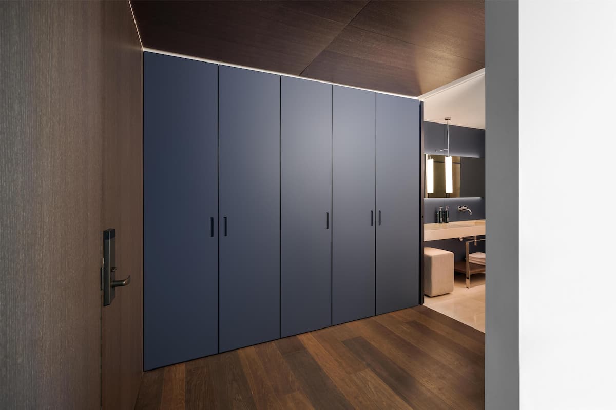 Une chambre moderne dotée d’une grande armoire, d’un plancher en bois et d’une salle de bain avec un miroir et un lavabo.
