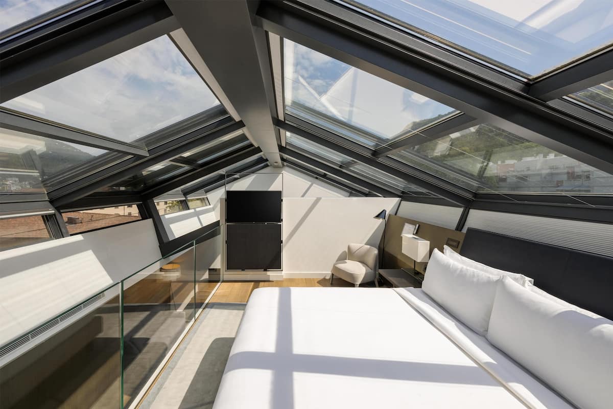 Une chambre d’hôtel moderne avec une lucarne, un lit, une chaise et une table de chevet.