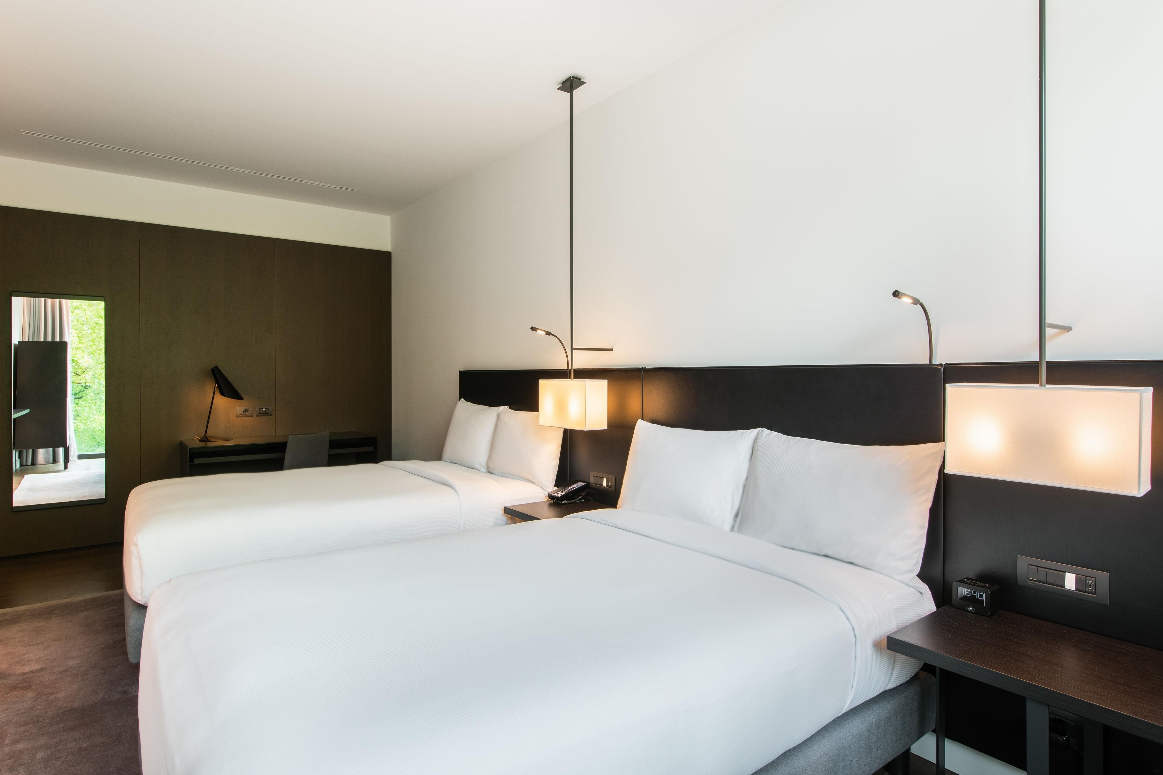 Hotellihuone, jossa on kaksi sänkyä, työpöytä, tuoli, lamppu ja yöpöytä, jossa on puhelin.