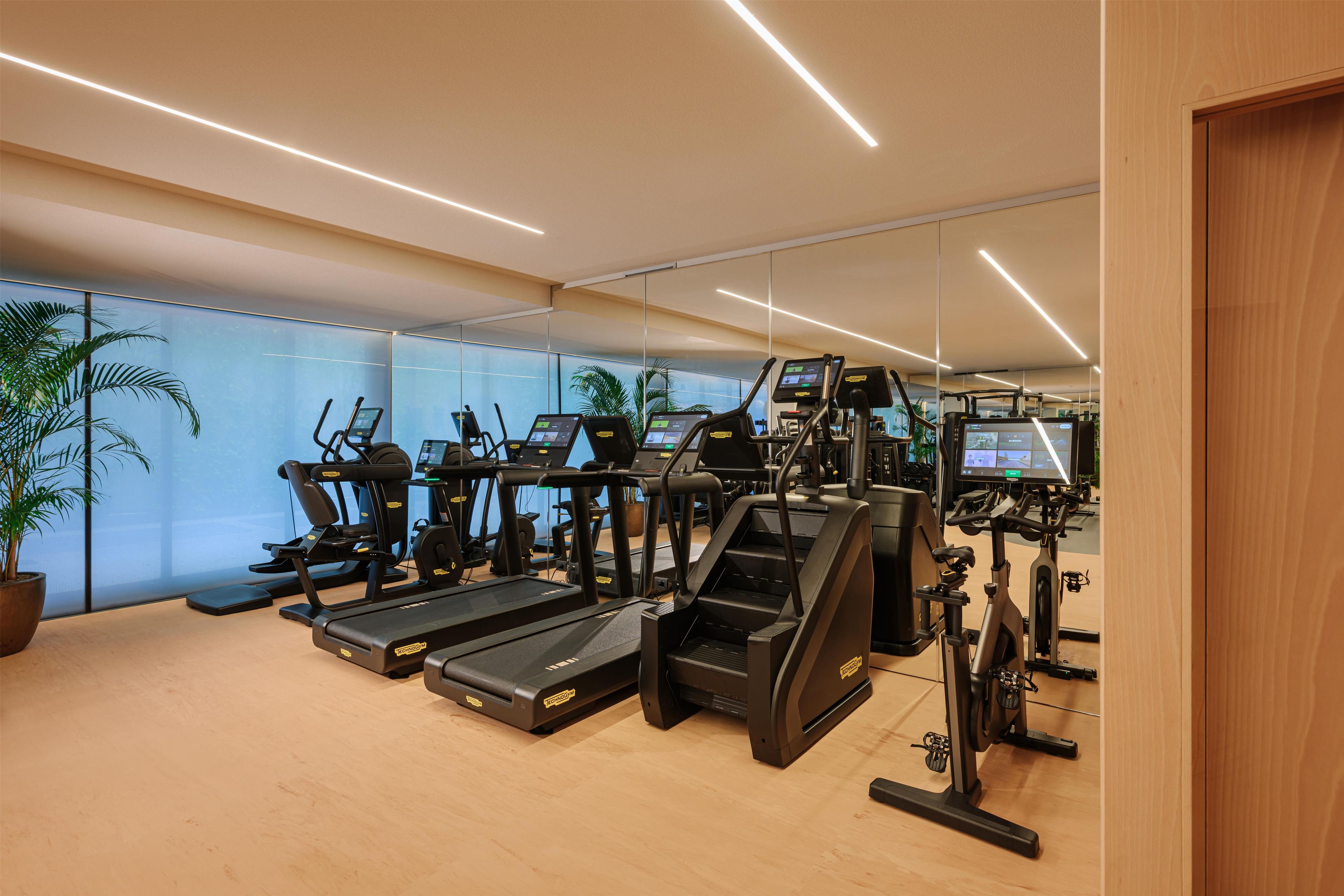 A gym with treadmills, ellipticals, and exercise bikes, featuring a modern design and glass walls.
