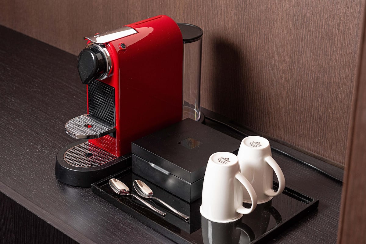 Une machine à café rouge avec un plateau, deux tasses blanches et une cuillère sur un plateau noir.
