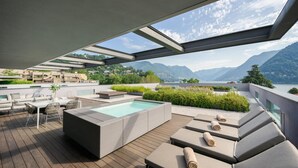A rooftop terrace with a hot tub, seating area, and a view of mountains and a lake. - Hilton Lake Como (Como)