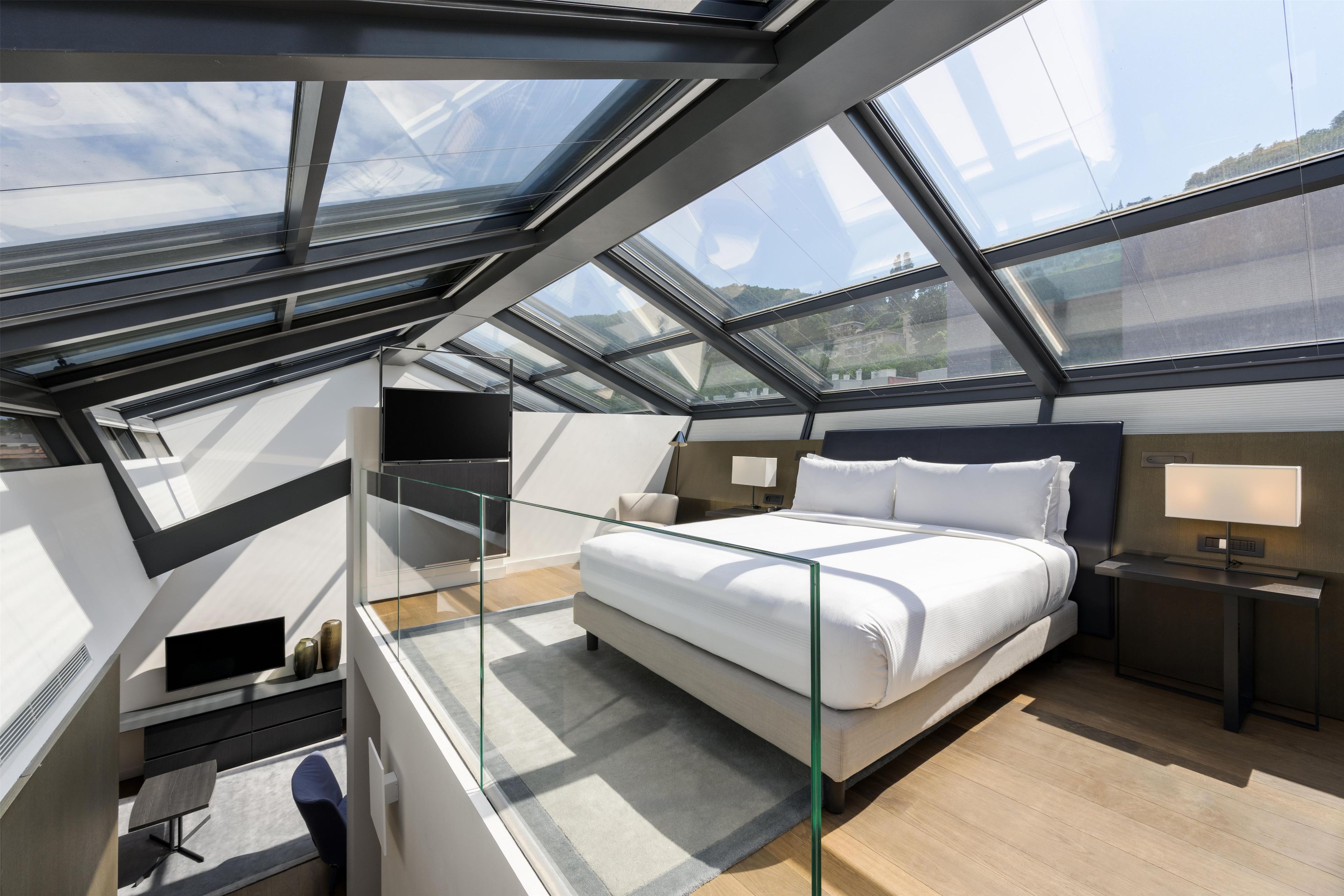 Une chambre à coucher moderne avec une lucarne, un lit, des tables de chevet et un bureau avec une chaise.