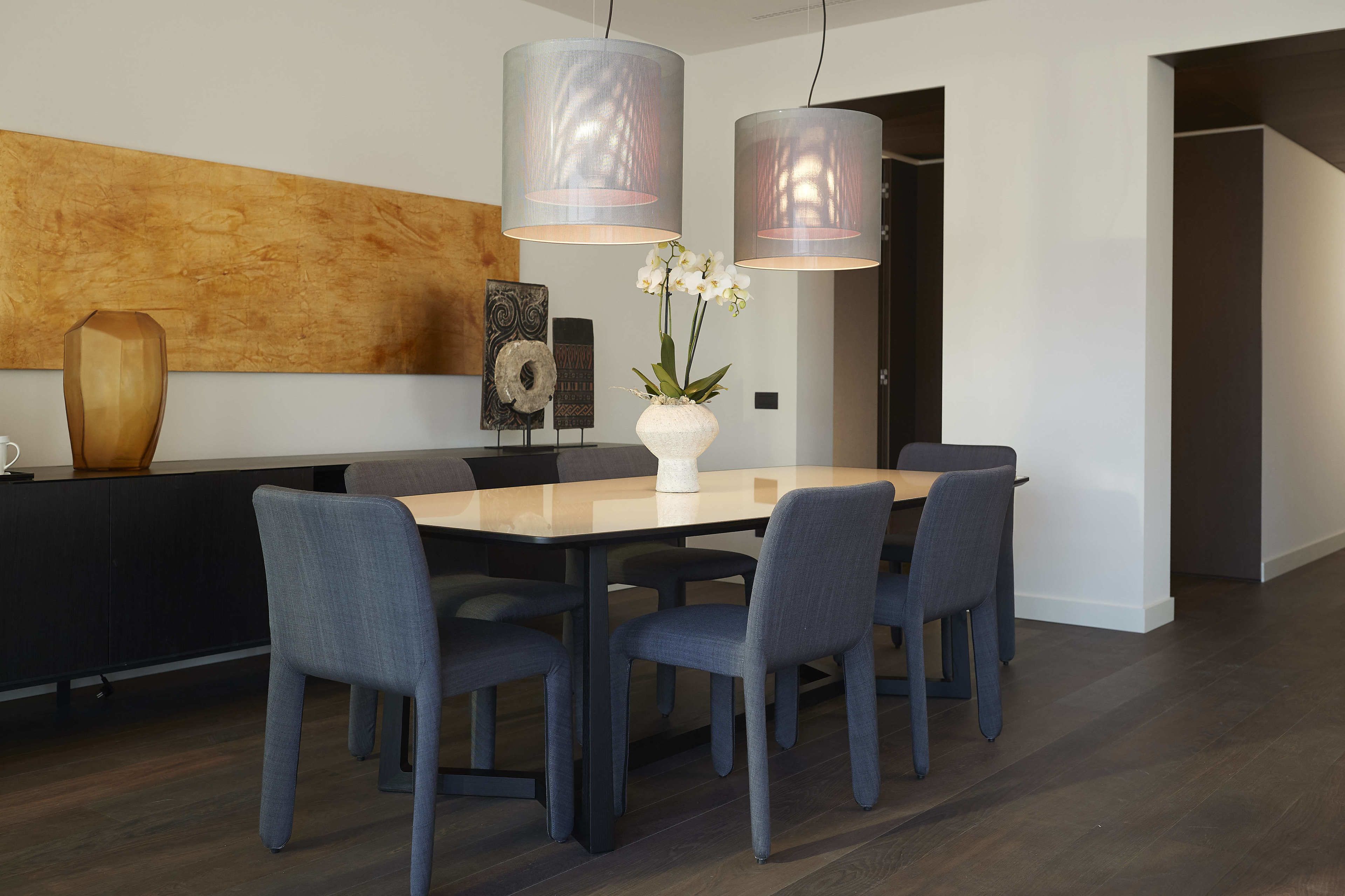 Un espace repas moderne avec une table rectangulaire, six chaises et deux lampes suspendues.