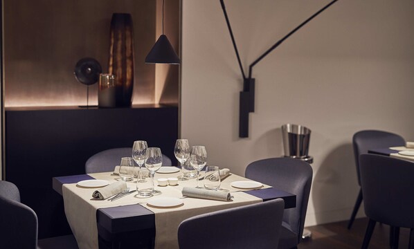 A modern dining area with a table set for four, including wine glasses, plates, and cutlery.