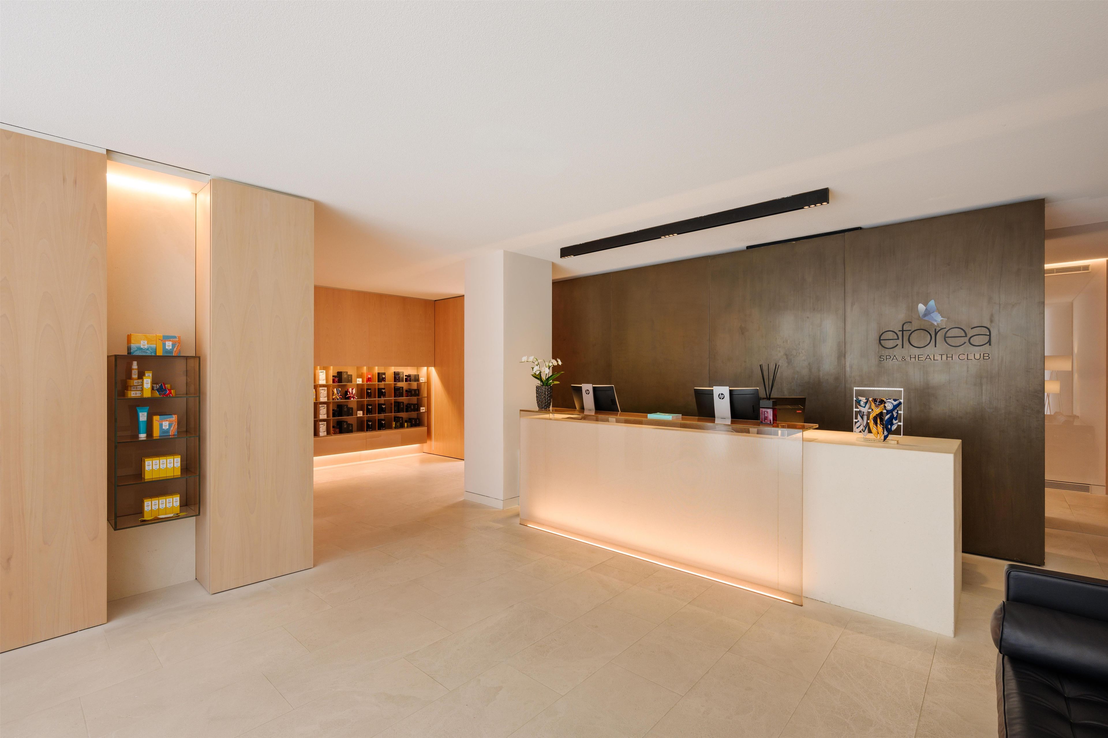 A reception area with a wooden reception desk, a glass display case with products, and a wall-mounted sign for 'eforea SPA & HEALTH CLUB'.