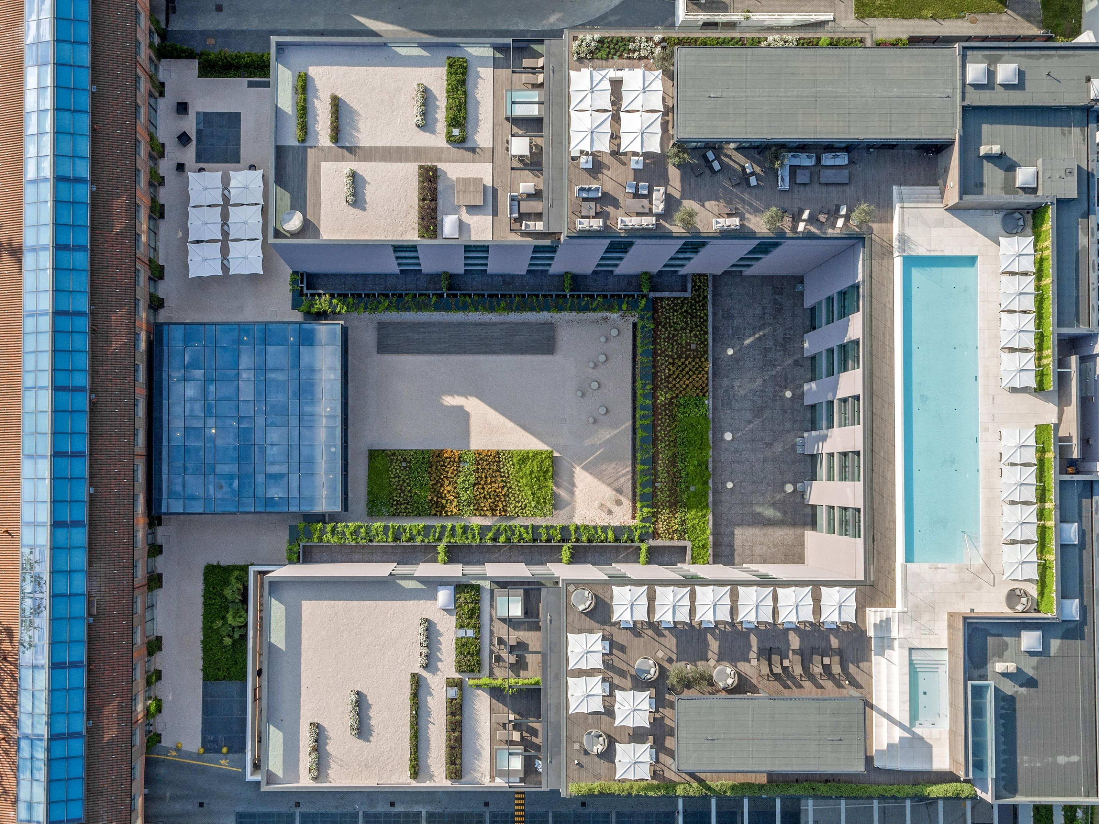An aerial view of a modern building with a rooftop pool, outdoor seating areas, and a mix of glass and concrete architecture.