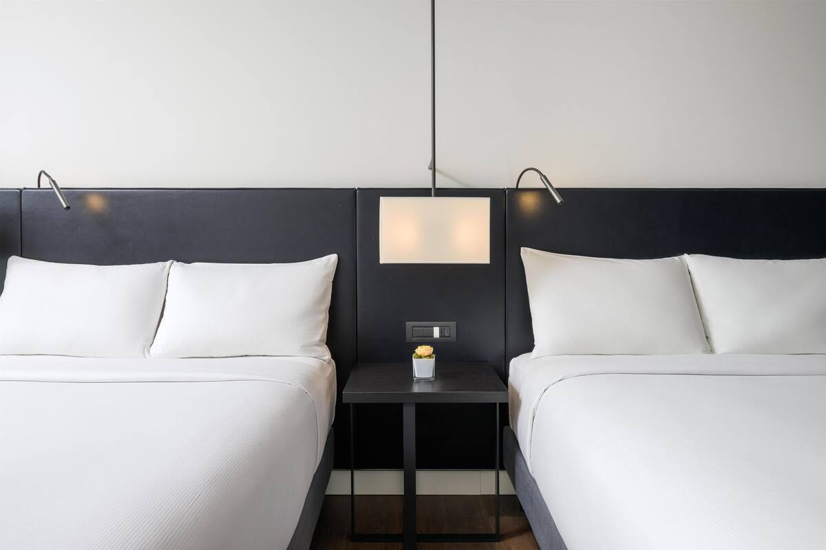 Une chambre d’hôtel avec deux lits, une table de chevet avec une lampe et une petite table ornée d’un vase de fleurs.