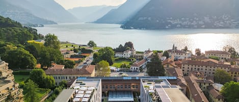 A hotel with a rooftop pool, surrounded by lush greenery and a view of a lake and mountains.