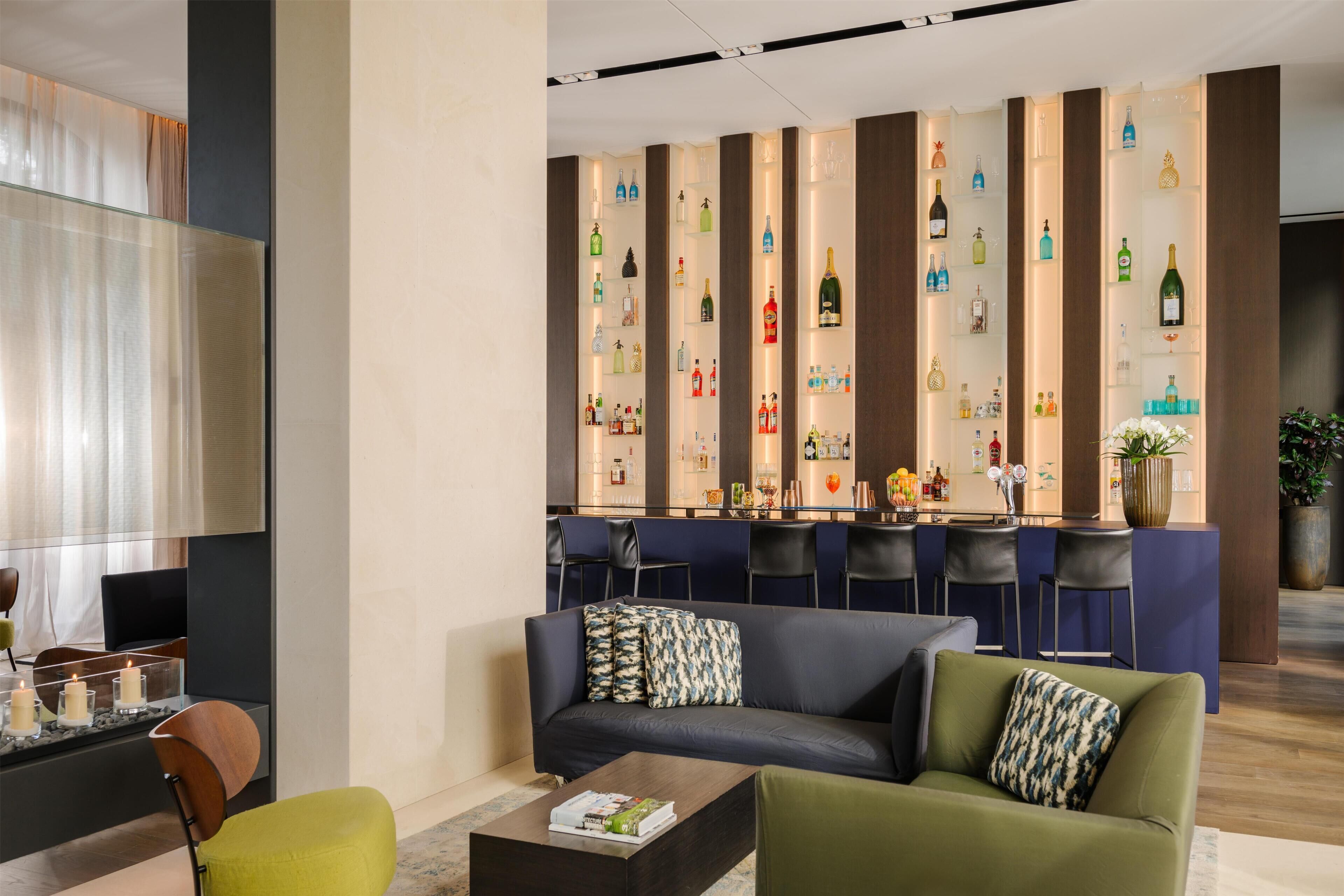 Un moderno vestíbulo de hotel con un área de descanso, un bar con mostrador y una pared decorada con diferentes botellas.