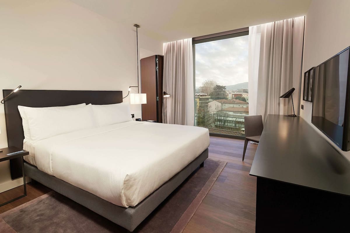 Une chambre d’hôtel avec un grand lit, un bureau, une chaise, une télévision et une vue sur la ville.
