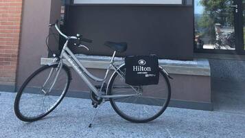 Ein Fahrrad mit schwarzer Tasche, das am Gepäckträger befestigt ist, steht auf einem Bürgersteig.