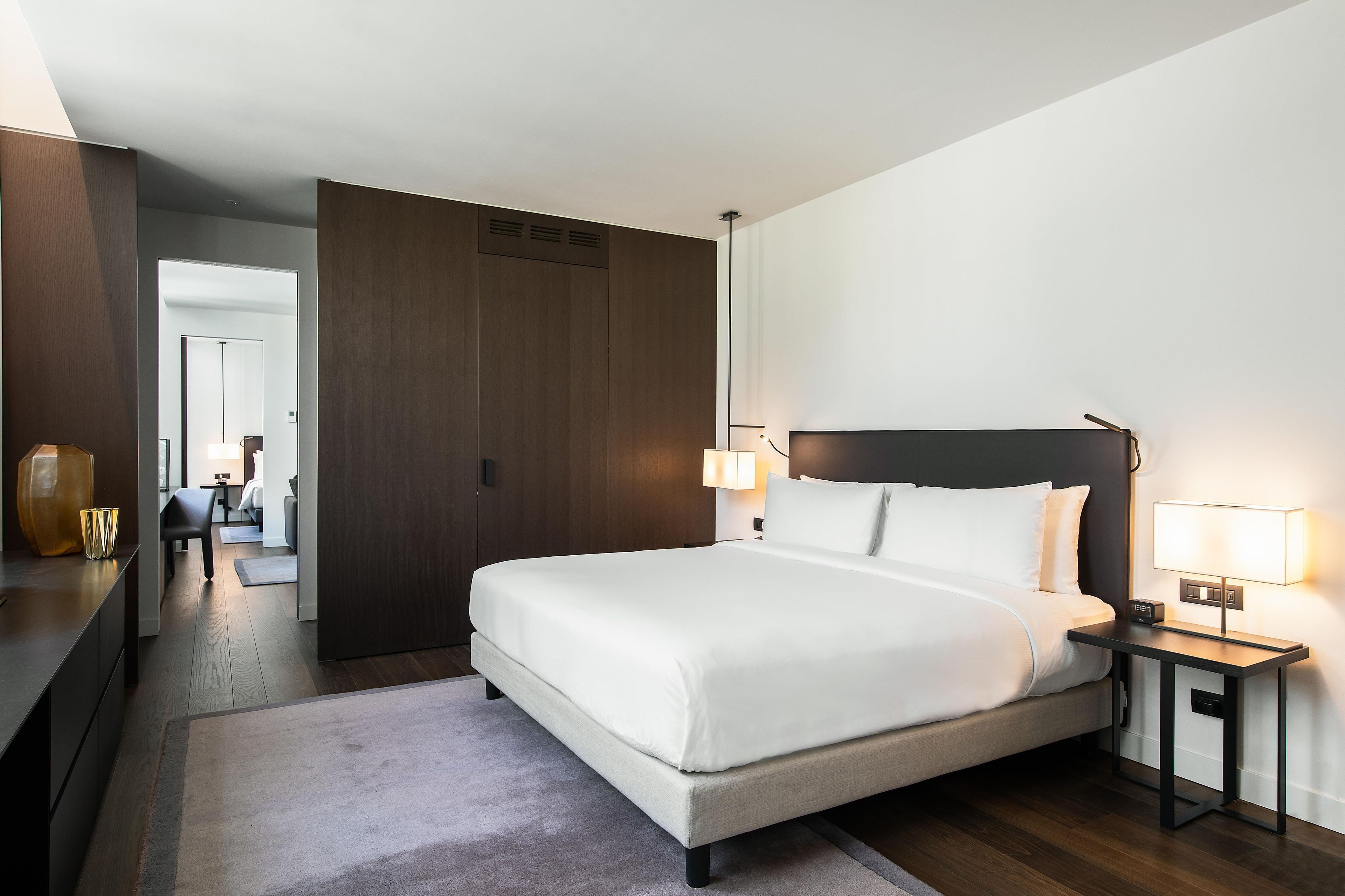 A hotel room with a large bed, bedside lamps, a nightstand, and a view into the hallway.