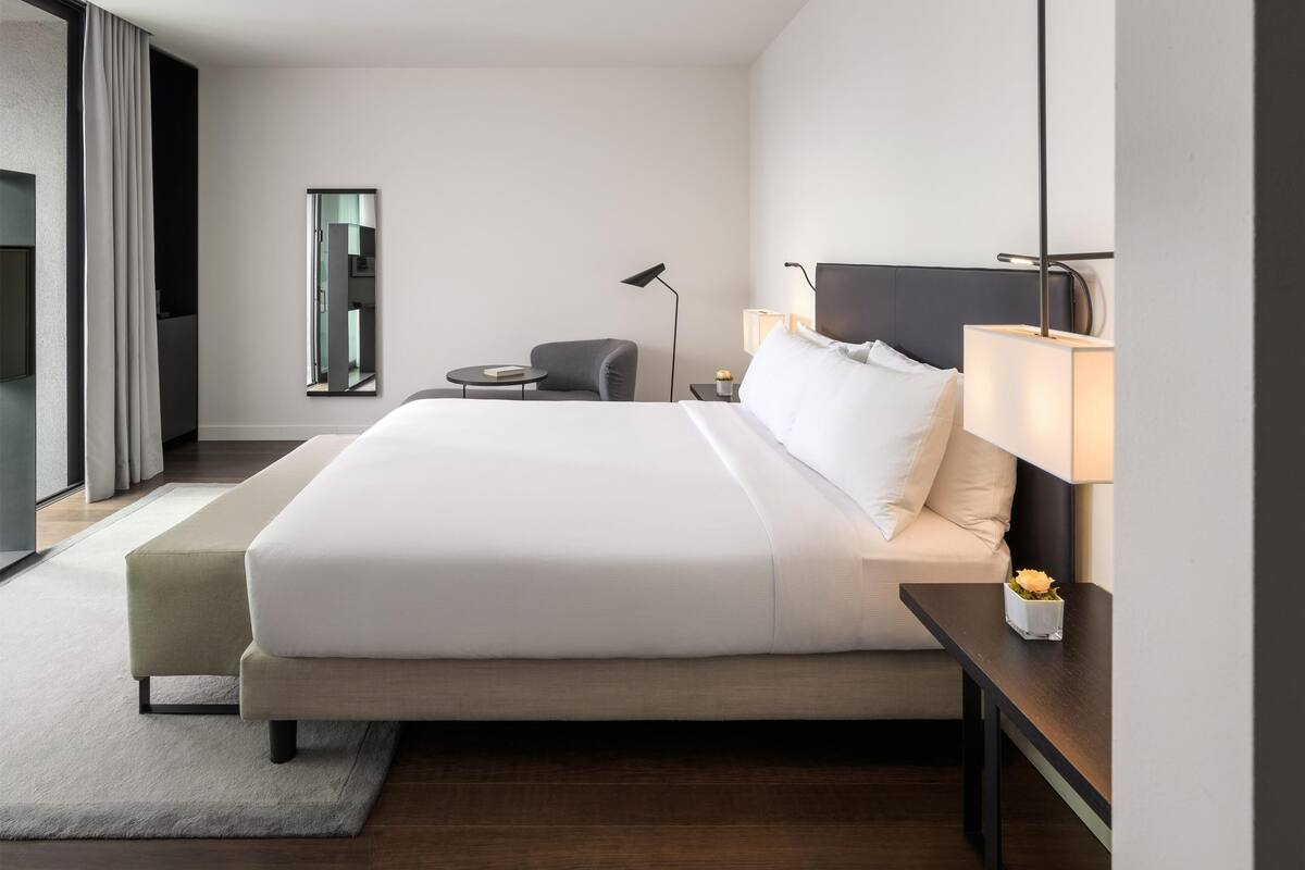 Une chambre d’hôtel moderne avec un grand lit, des tables de chevet, un bureau, une chaise, une lampe et une fenêtre.