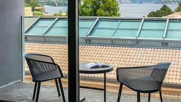 A balcony with a view of mountains and a lake, two black chairs, and a small table.