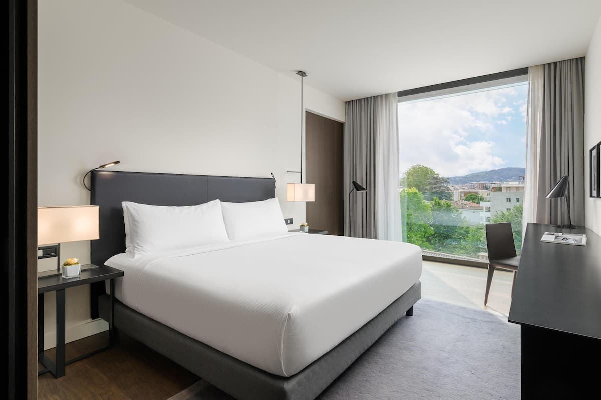 Une chambre d’hôtel moderne avec un grand lit, des tables de chevet, un bureau et une vue sur la ville.