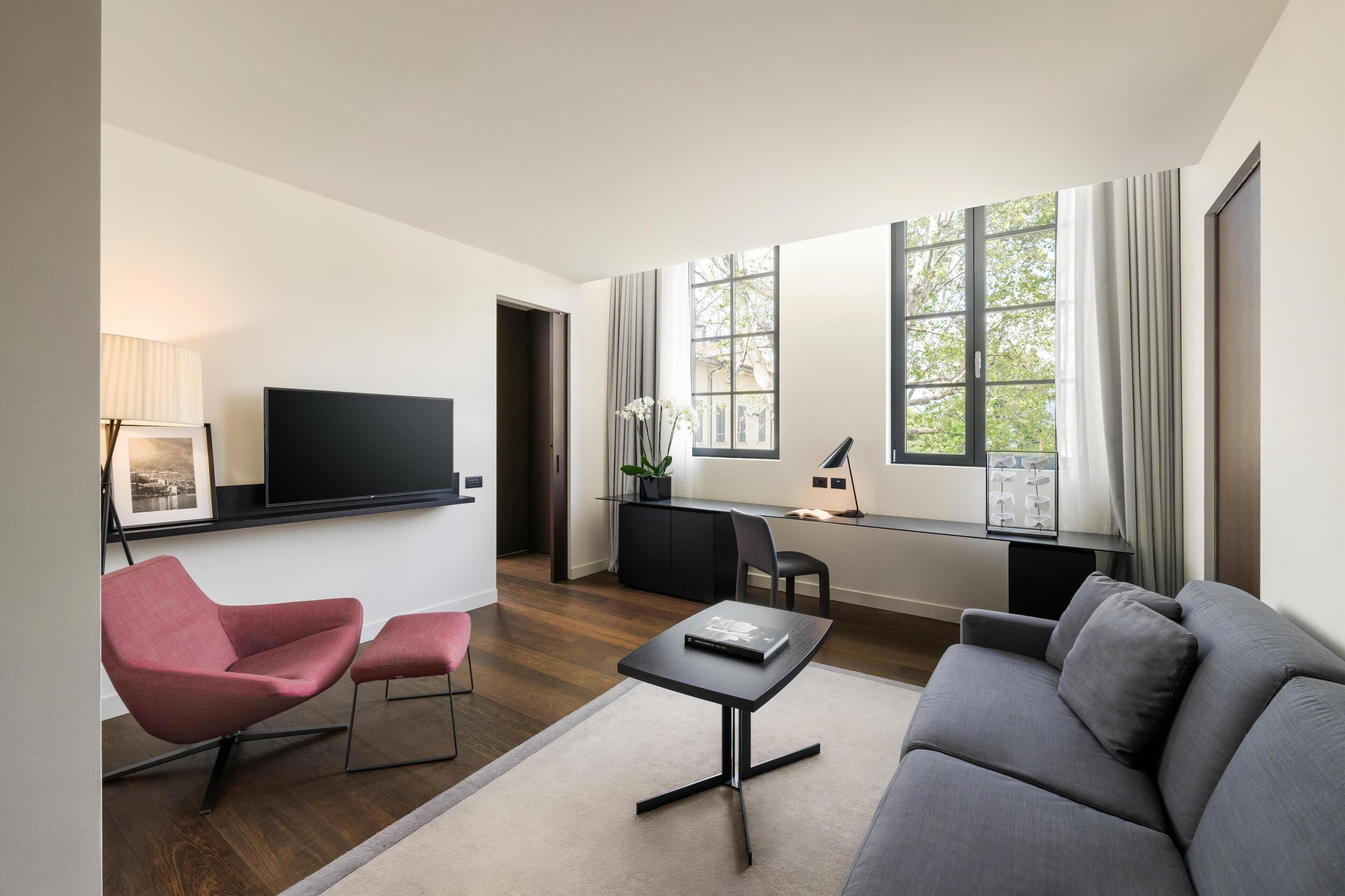 A modern living room with a flat-screen TV, a sofa, a chair, a small table, and a desk with a computer.