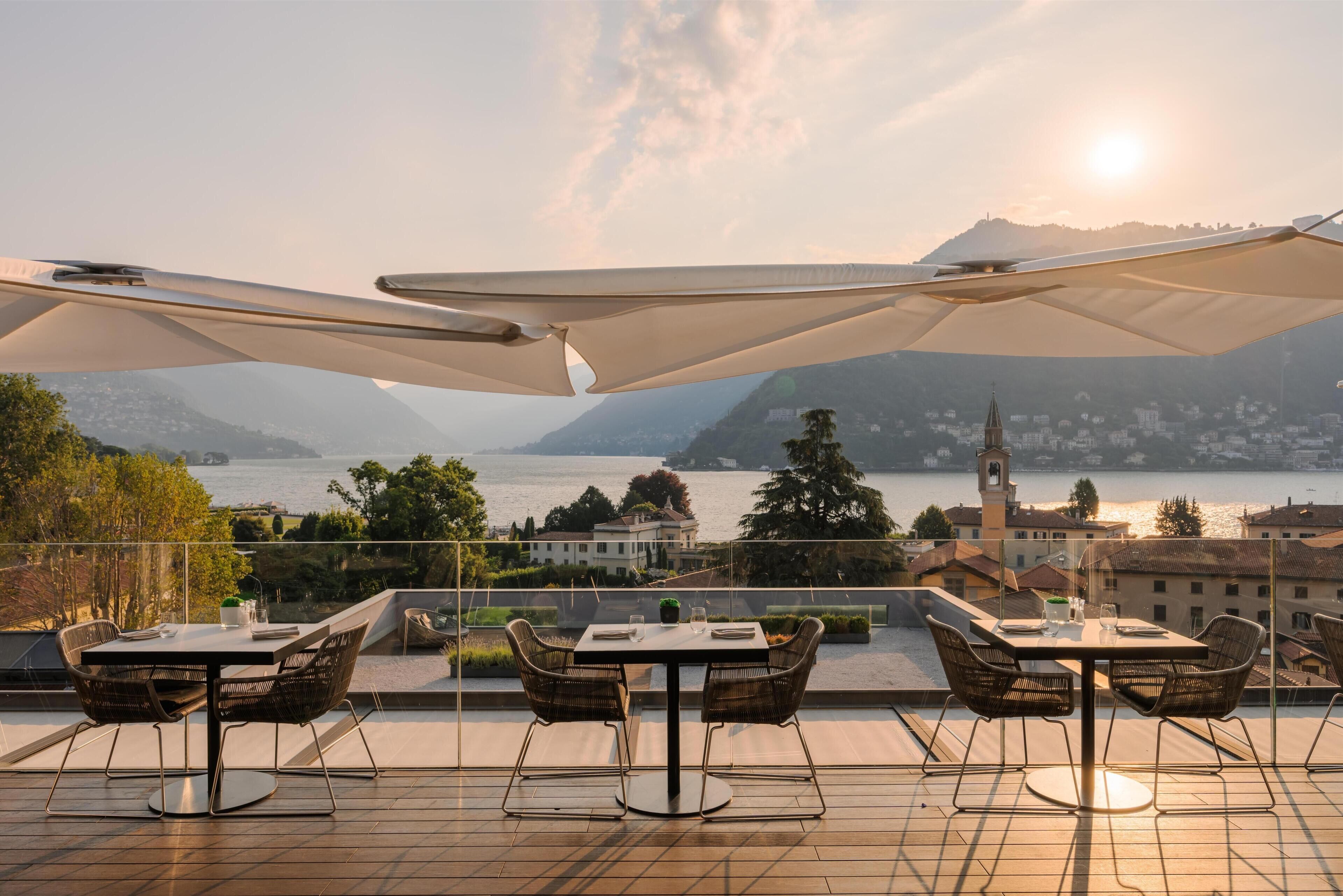 Una terrazza con tavoli e sedie, affacciata su uno specchio d'acqua e sulla città.