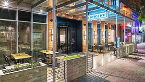 An outdoor cafe area with tables and chairs, a wooden planter with greenery, and a sign for 'caroline'. - Aloft by Marriott Austin Downtown (Austin)