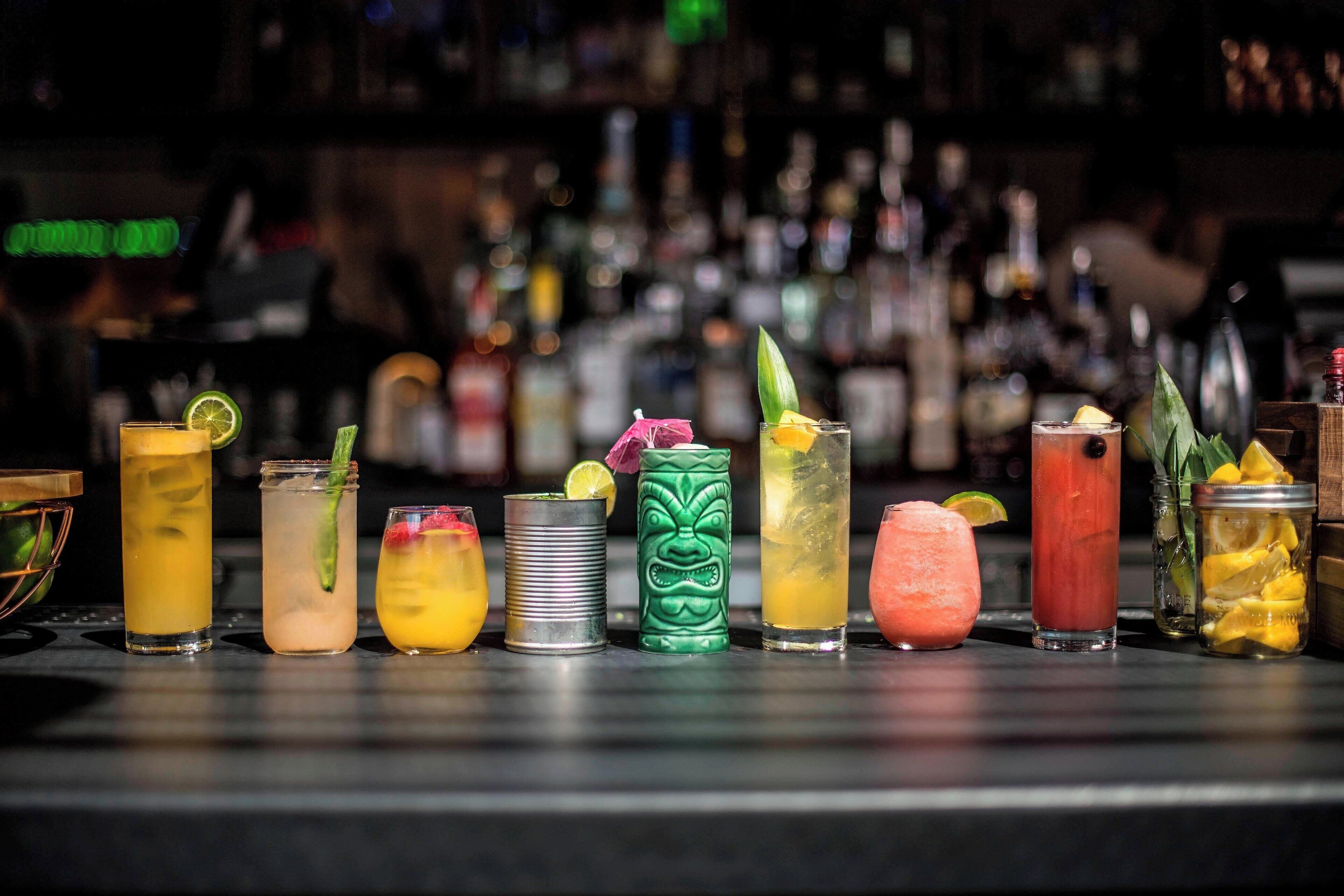 Un bar avec un comptoir proposant divers cocktails et des bouteilles en arrière-plan.