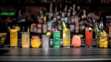 Un bar avec un comptoir proposant divers cocktails et des bouteilles en arrière-plan.