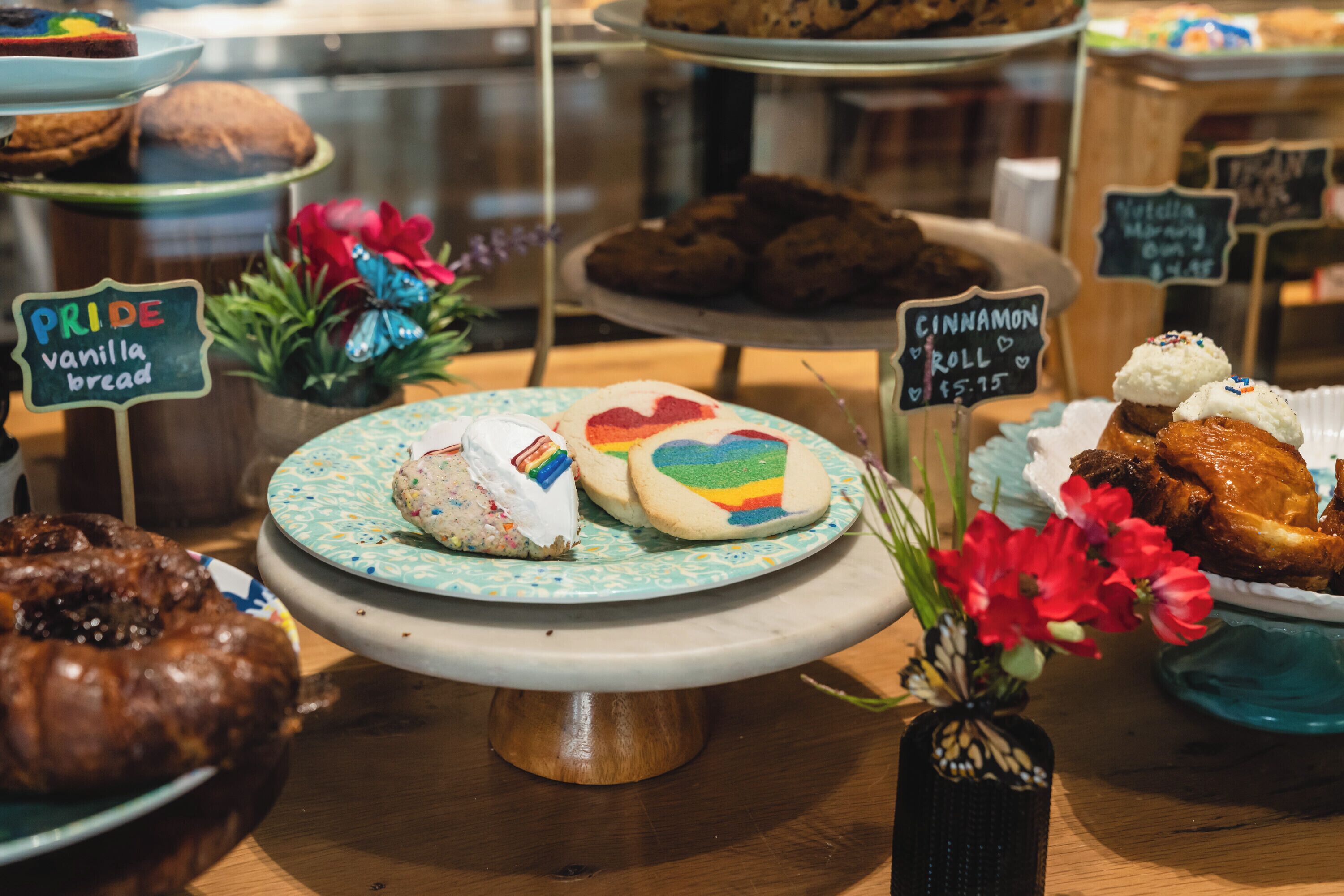 A bakery display with various baked goods, including a rainbow heart cake and cinnamon roll.