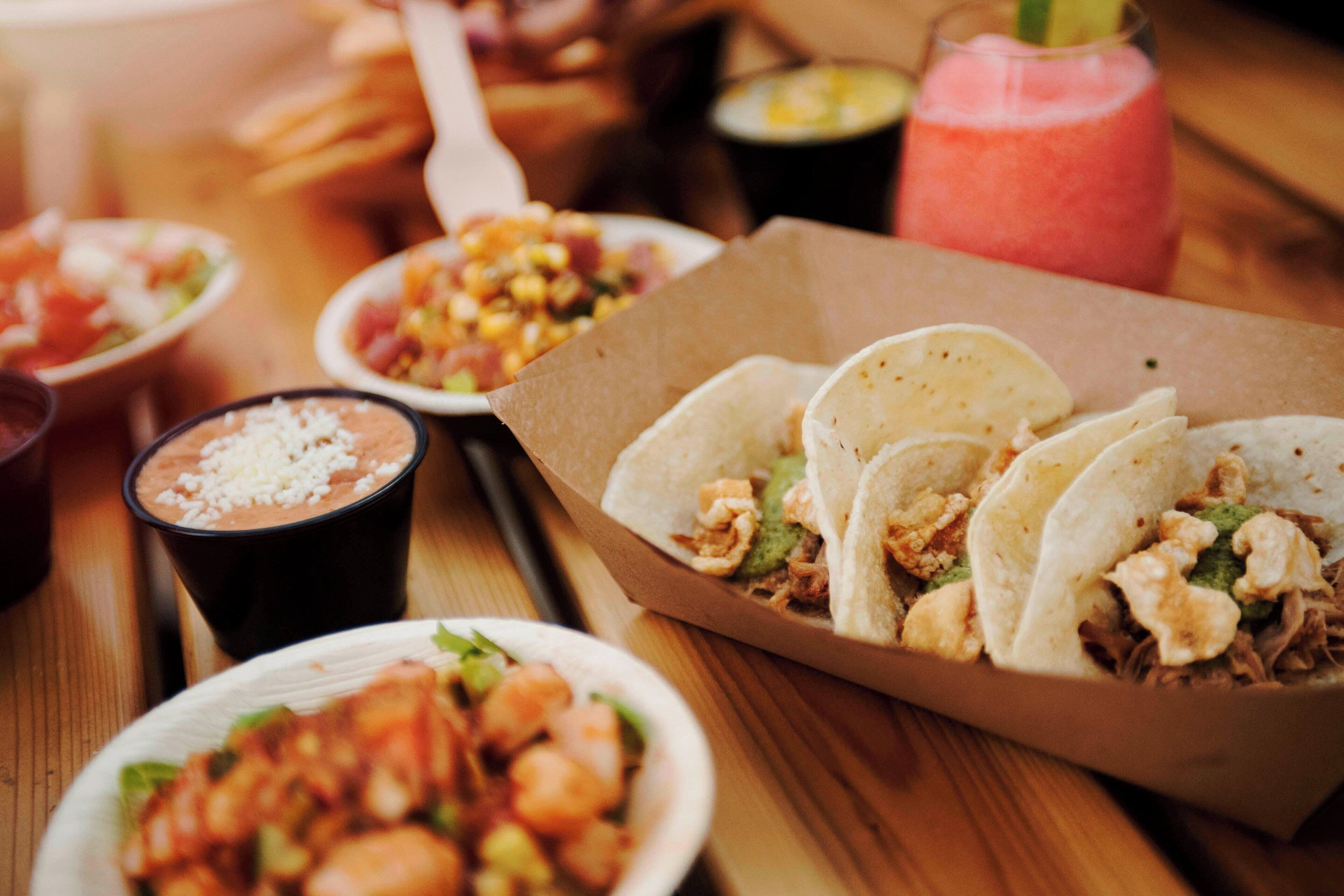 A variety of food items including tacos, a bowl of shrimp, and a smoothie on a wooden table.