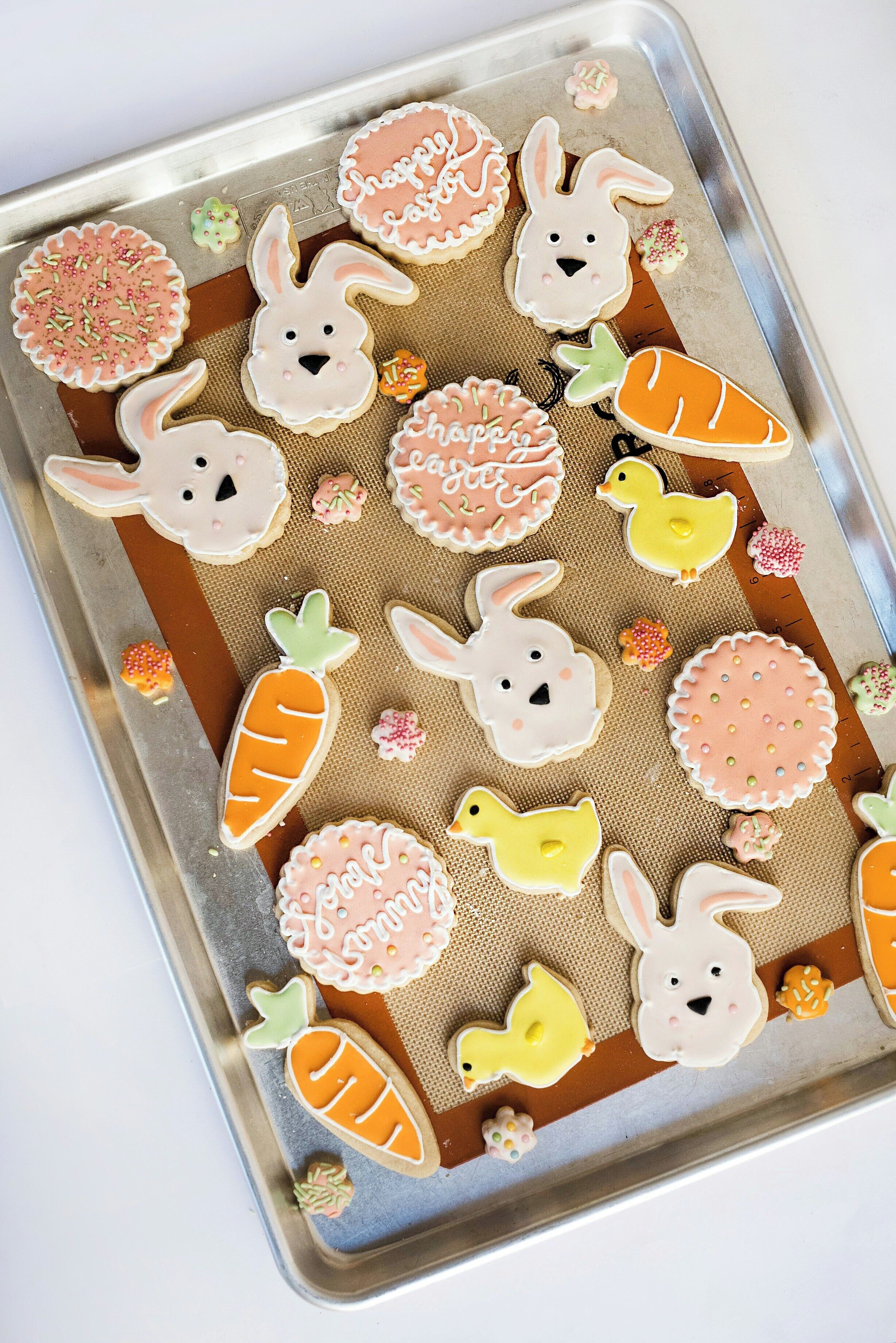 Uma bandeja de biscoitos decorados com coelhos, cenouras e flores.