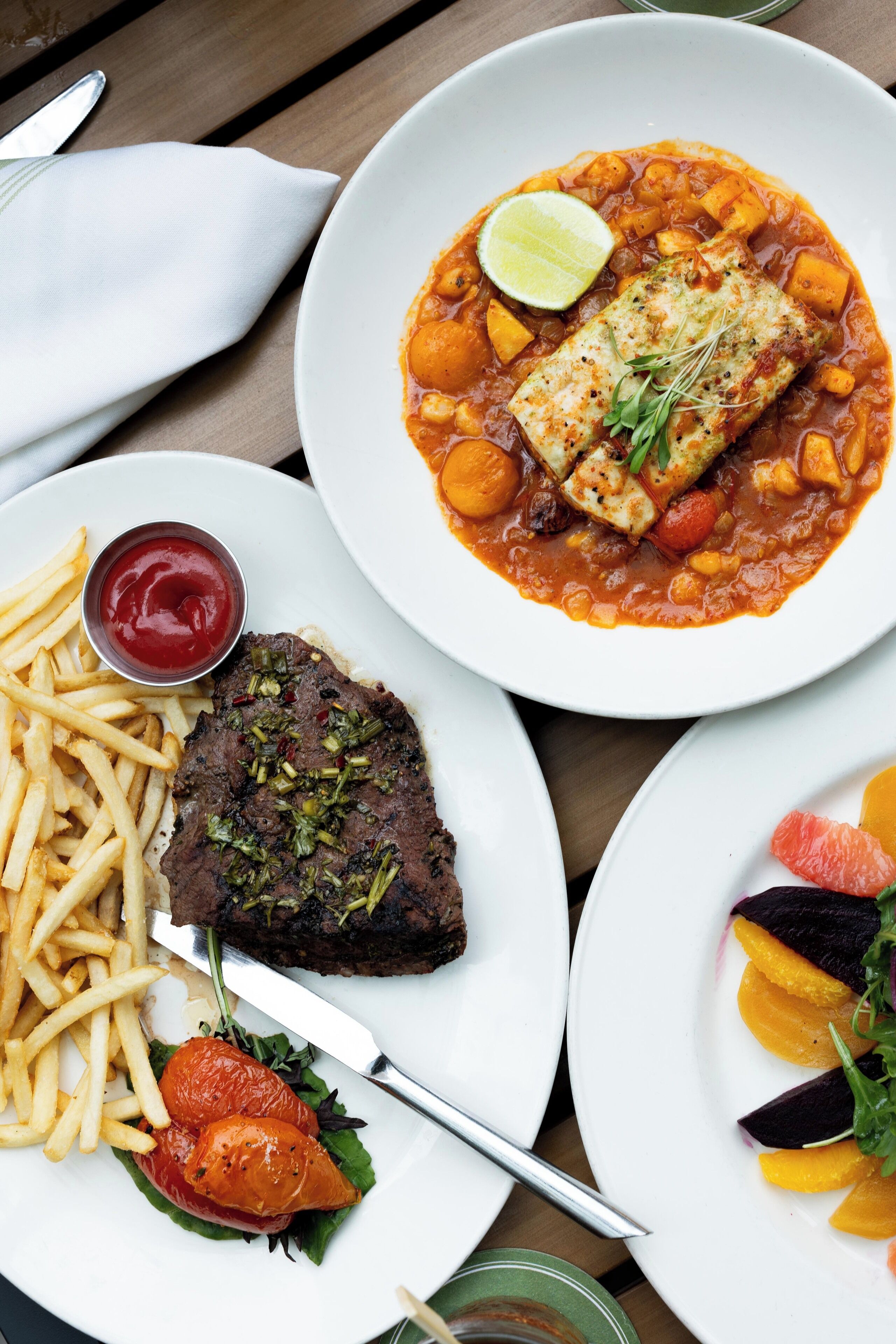 Een tafel met diverse gerechten, waaronder vis, steak, friet en een salade.