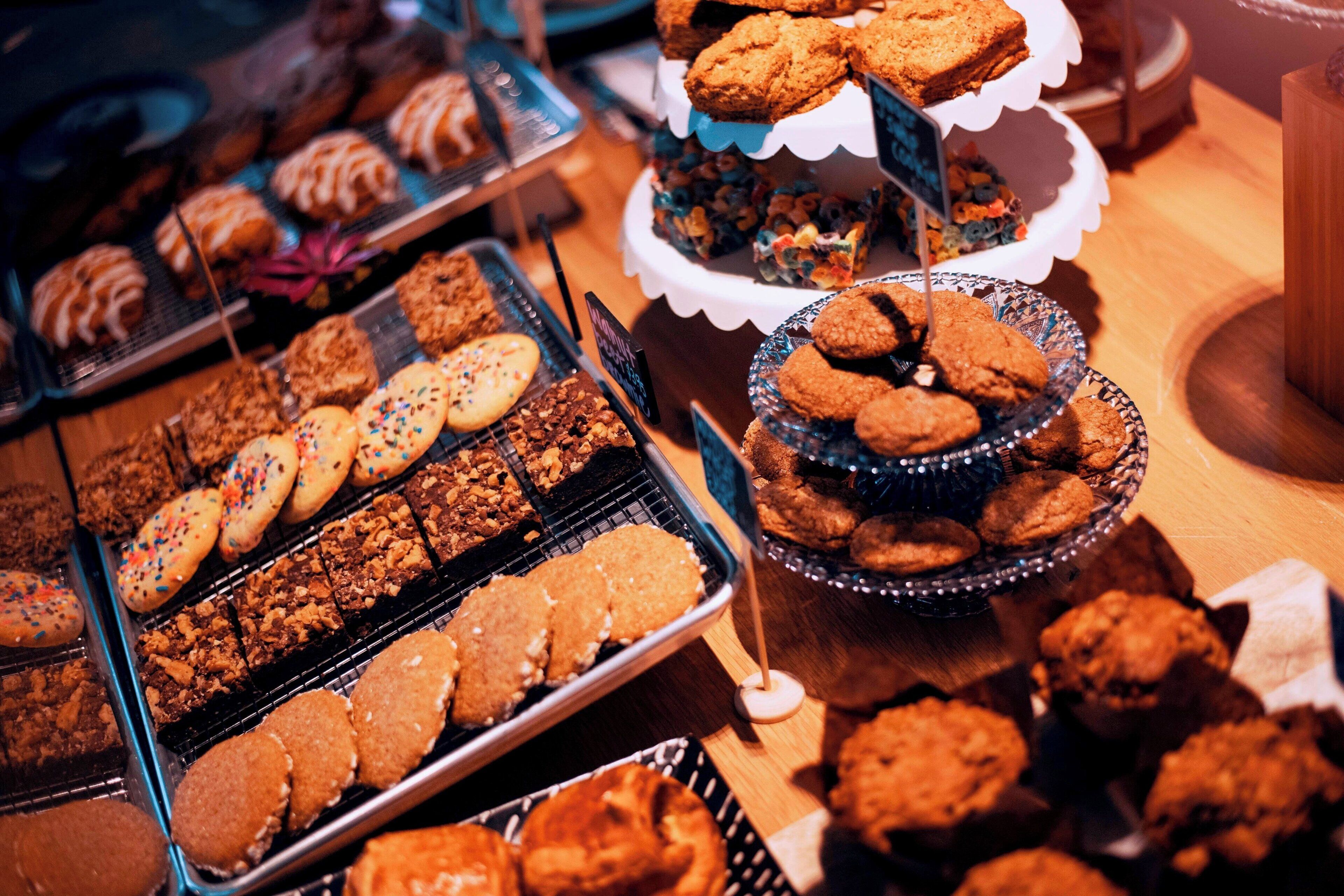 Diversas opciones de productos horneados expuestos en bandejas y soportes, entre ellos galletas y brownies.