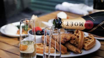 Una botella de Moët champagne siendo servida en una copa sobre una mesa de madera, con gofres y un plato de comida al fondo.