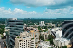 A cityscape with modern and historic buildings, a clear sky, and a distant view of greenery.