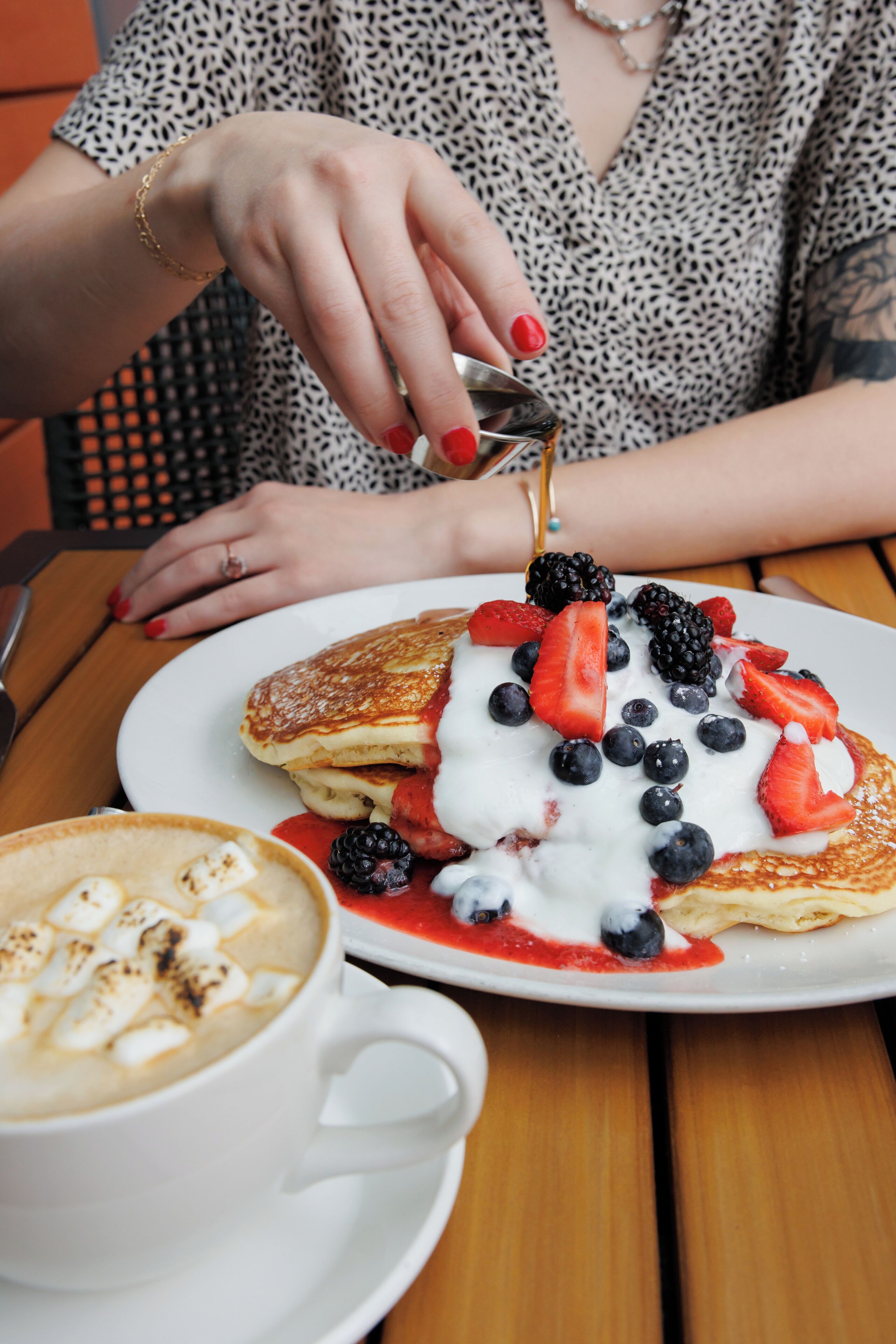 A person serving pancakes with whipped cream and berries on a plate.