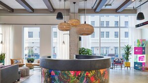 A modern hotel lobby with a central reception desk, large windows, and a view of the cityscape. - Aloft by Marriott Austin Downtown (Austin)