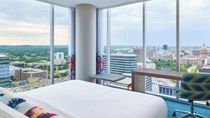 A hotel room with a large bed, a desk, and a chair. The room has large windows offering a city view. - Aloft by Marriott Austin Downtown (Austin)