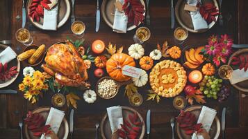 A Thanksgiving table set with a roasted turkey, pumpkins, and autumn leaves.